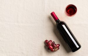 Wine bottle, grape and glasses on white textile background, copy space, top view