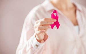 Close up of woman holding pink ribbon for breast cancer awarness. Detail of female hand holding pink awareness ribbon. Young woman supporting living with women's breast tumor.
