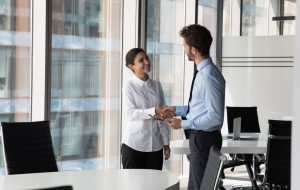 Two diverse confident business man and woman shaking hands in office meeting room. Employer hiring candidate after job interview. Client greeting manager, lawyer with handshake. Negotiation concept