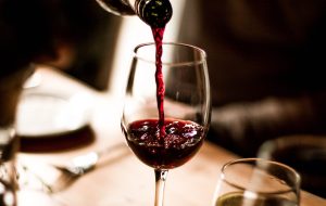 Red wine being poured into a stem glass at the table.