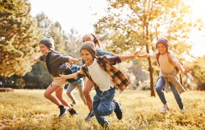 Group of happy joyful school kids with backpacks running with outstretched arms in forest on sunny spring day, excited children scouts boys and girls having fun during camping activity in nature