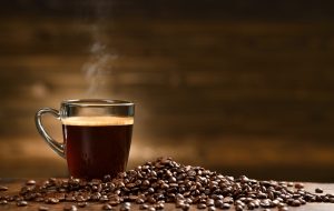 Cup glass of coffee with smoke and coffee beans on old wooden background