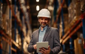 Manager with safety helmet holding digital tablet in warehouse