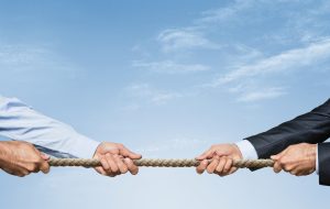 Two businessman pulling a rope in opposite directions over sky background with copy space