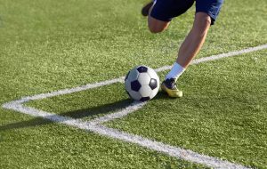 Footballer is preparing to give a corner kick with the ball on the goal on the green grass, playing on the football field.