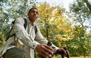Young african american man with backpack riding bike in spring nature, bottom view. Work in nature concept