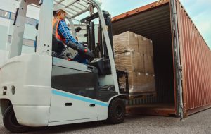 Forklift Driver Loading a Shipping Cargo Container with a Full Pallet with Carboard Boxes in Logistics Operations Port Terminal.