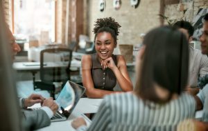 We are one team! Young and cheerful afro american woman smiling while having a meeting with colleagues in the modern office. Business concept