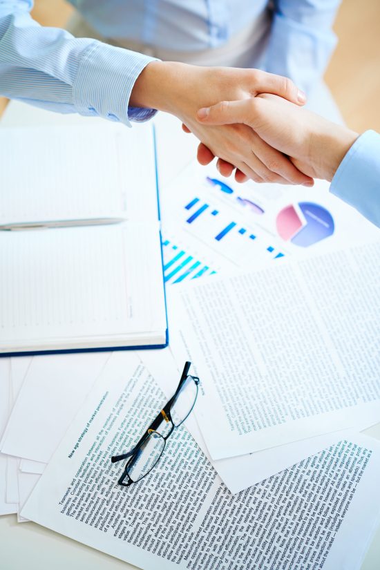 Close-up of female and male handshaking over workplace with business documents