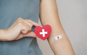senior human hand holding red paper heart shape and red blood drop symbol on bandage for world blood donation and donor day and save life concept