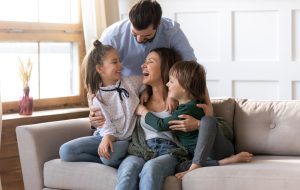 Happy young Caucasian family renters with two small kids sit rest on couch in cozy living room. Smiling parents with little children relax on sofa enjoy weekend in new renovated design home together.