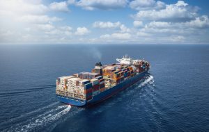 A large container cargo ship travels over calm, blue ocean